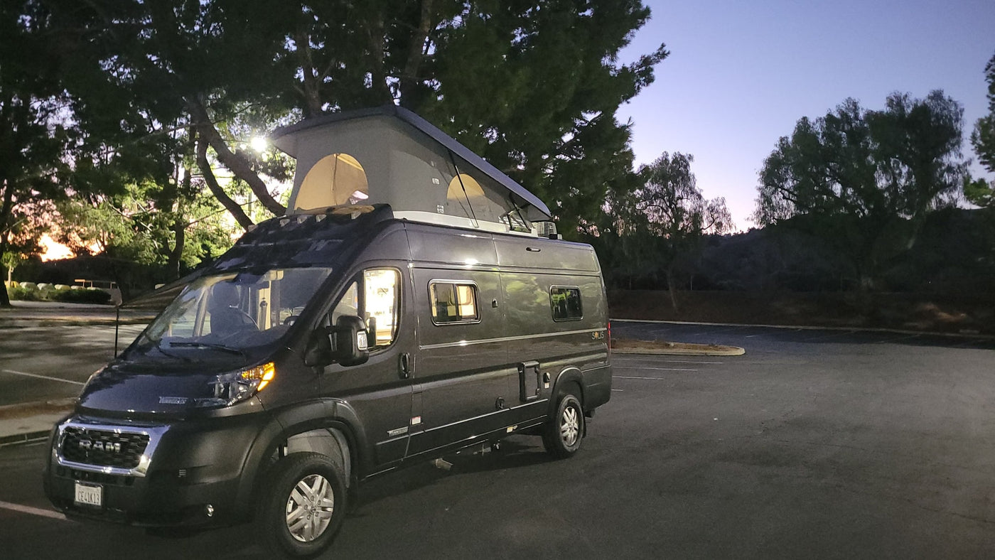 Modern grey pop-top RV rental camper van (Winnebago Solis) parked at dusk, interior lit. — photo 13