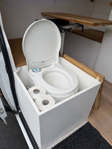 Essential for your RV rental: a clean Thetford portable toilet with lid open, neatly stored with toilet paper in a campervan.