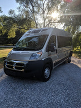Tan rv rental van parked on a gravel driveway with sunlit trees. Ideal for your next outdoor adventure.