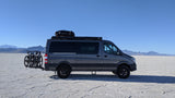 Explore with an RV rental! Gray van with bikes on vast white salt flats, mountains in distance, clear blue sky.