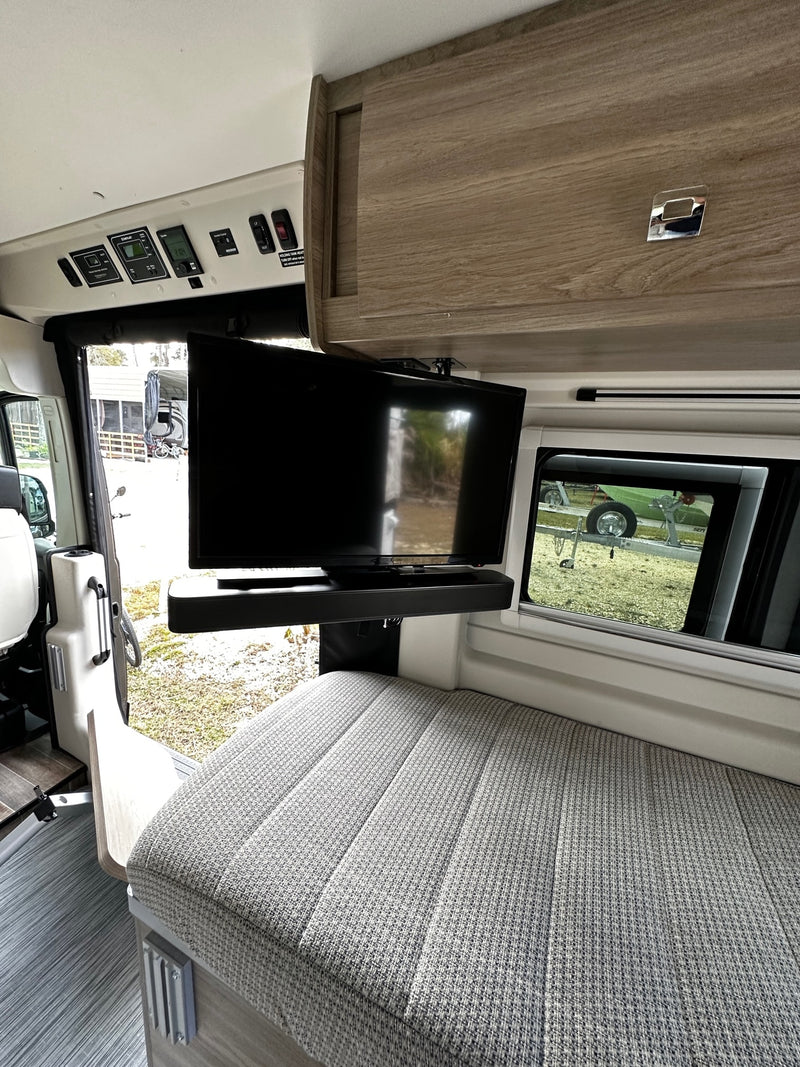 RV rental: Interior shows a swiveling TV, system controls, and upholstered seating/bed. Outside, a trailer is visible. — photo 15