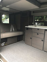 Inside this modern **rv rental**: a comfortable bench seat, compact kitchen with sink, microwave, and stylish dark cabinets.