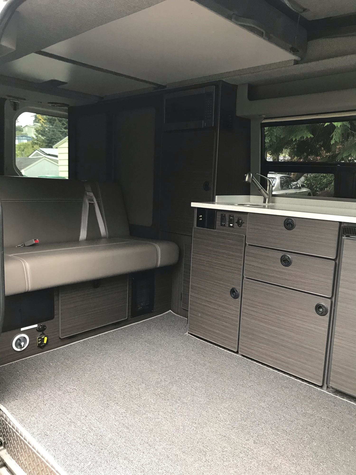 Inside this modern **rv rental**: a comfortable bench seat, compact kitchen with sink, microwave, and stylish dark cabinets.