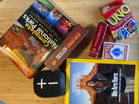 Packing for an RV rental trip: National Parks guide, games (UNO, Exploding Kittens), & a speaker for onboard fun.