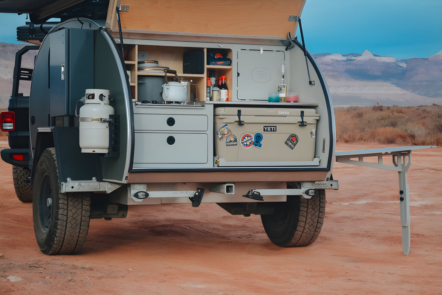 This compact RV rental trailer's open rear kitchen has a stove, sink, and Yeti cooler, ready for desert adventures.