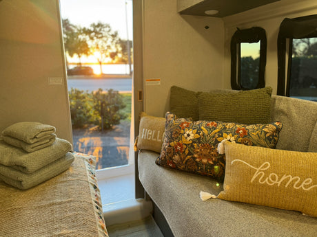 Cozy rv rental interior with decorative pillows, stacked towels, and an open door revealing a scenic sunset view.