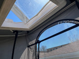 View from an RV rental: Bright blue sky seen through an open skylight and a mesh window, revealing a rooftop.