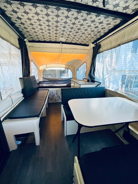 Inside a cozy pop-up camper, perfect for an RV rental. Features dining seating, sleeping areas, and a decorative ceiling.