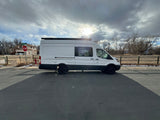 White camper van, resembling an RV rental, parked on a road under a sunlit, cloudy sky.