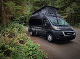 Dark grey camper van with pop-top extended, parked by lush forest. Your ideal rv rental for nature adventures.