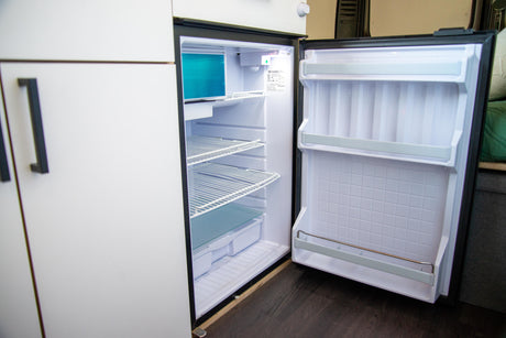 Inside an RV rental, this compact refrigerator is open, revealing its empty shelves, freezer, and door storage.