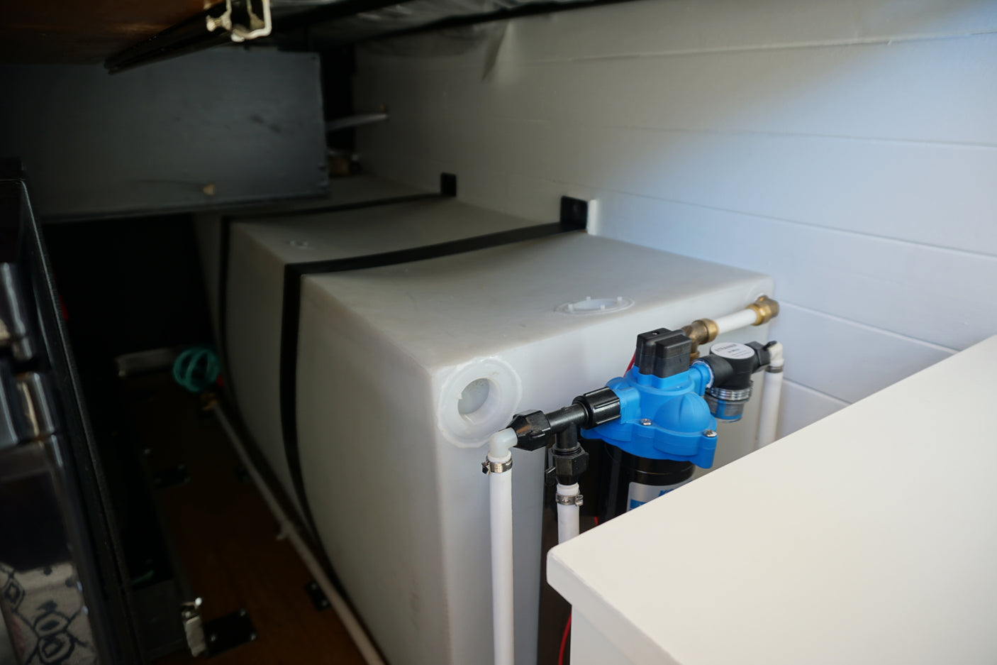 RV rental: Large white water tank, blue pump, and filter system plumbed in a compact utility space.