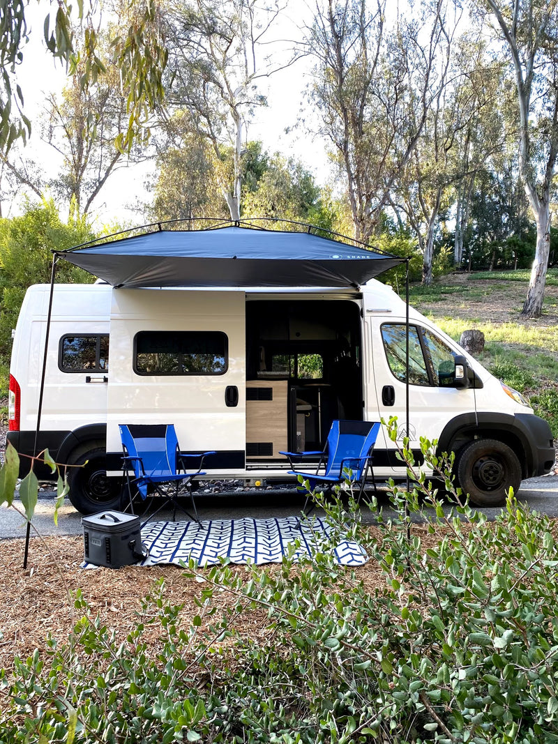 Scenic rv rental setup: White camper van with awning, blue chairs, and cooler, ready for outdoor comfort in nature. — photo 2