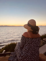 Person in a straw hat & floral dress on a bench, admiring a serene ocean sunset. Ideal calm after an RV rental journey.