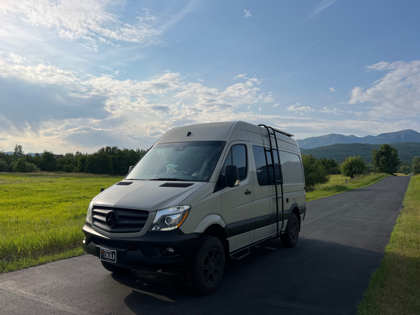 Cream Mercedes Sprinter RV rental, with roof ladder, parked on asphalt road in scenic mountains. — photo 3