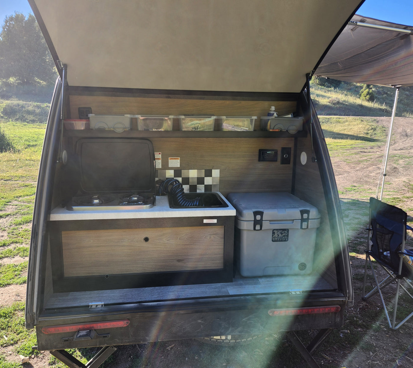 RV rental teardrop camper outdoor kitchen. View inside the rear hatch with stove, sink, cooler, and storage. Perfect for camping. — photo 10
