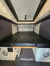 Inside a compact RV rental, featuring a comfortable convertible bed, pop-top roof, and integrated controls.