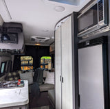 Bright, modern rv rental interior showcasing a compact kitchen with stove, cozy seating area, overhead control panel, microwave, and fridge.