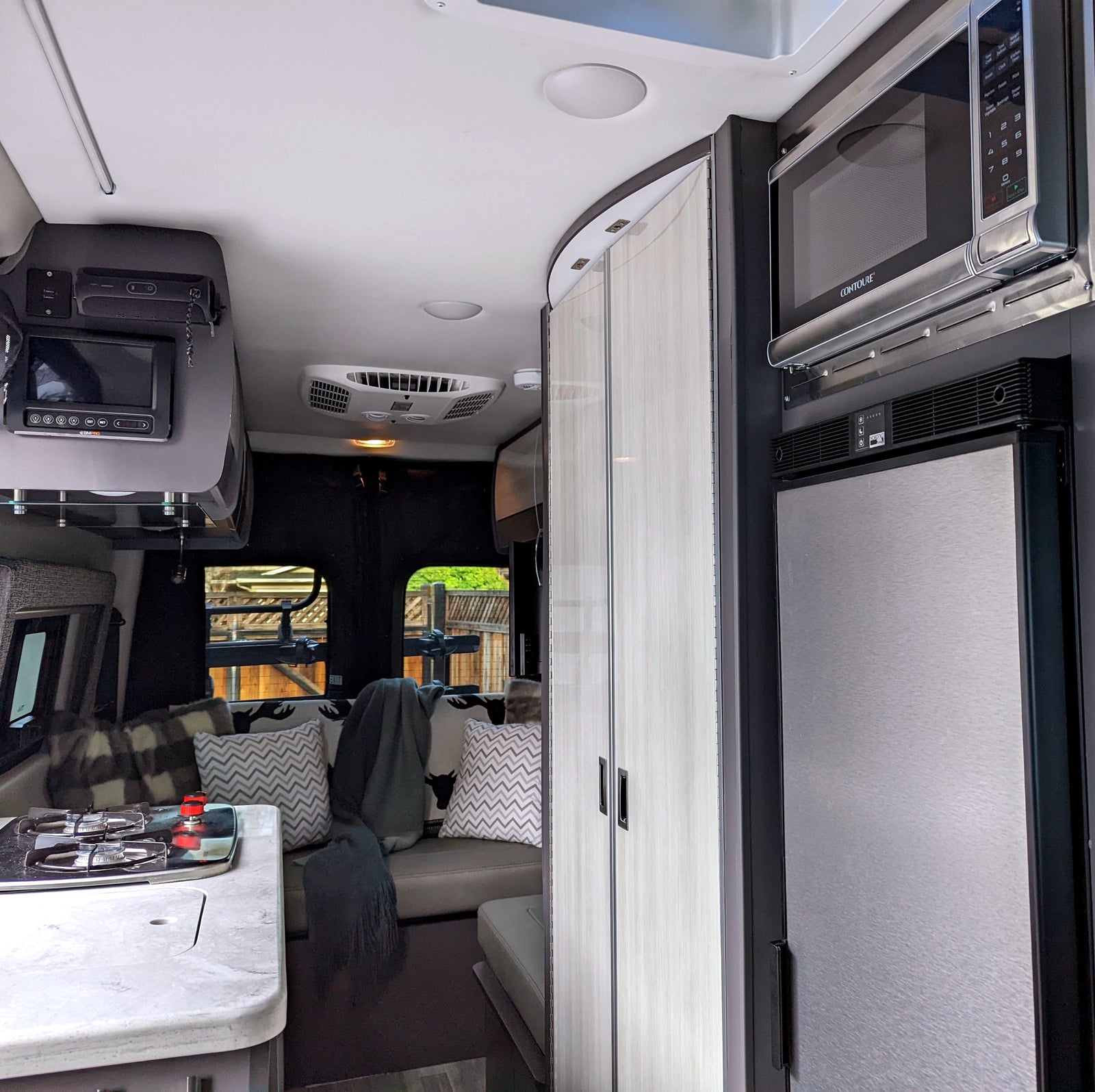 Bright, modern rv rental interior showcasing a compact kitchen with stove, cozy seating area, overhead control panel, microwave, and fridge.