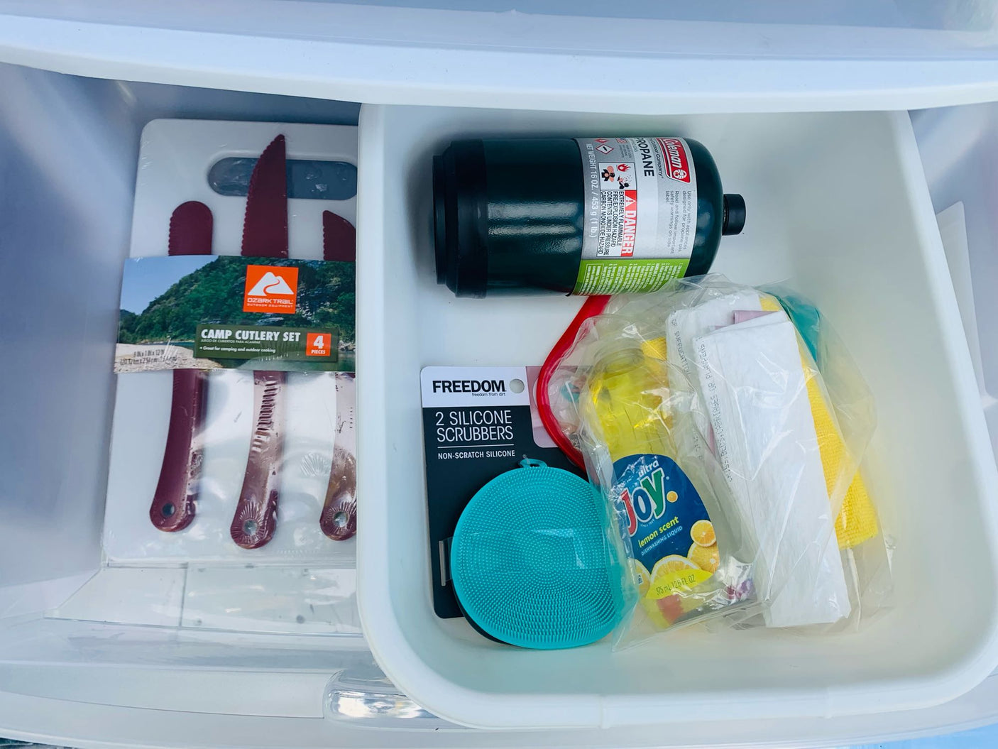 Organized RV rental drawer: camp cutlery, propane, dish soap, scrubbers, and cleaning cloths for a smooth trip.