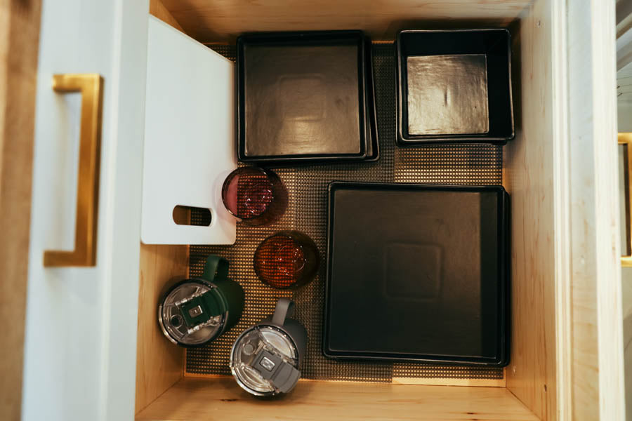 Organized **rv rental** drawer with black trays, tumblers, cutting board, and cups on a liner. Efficient kitchen storage for your adventure.