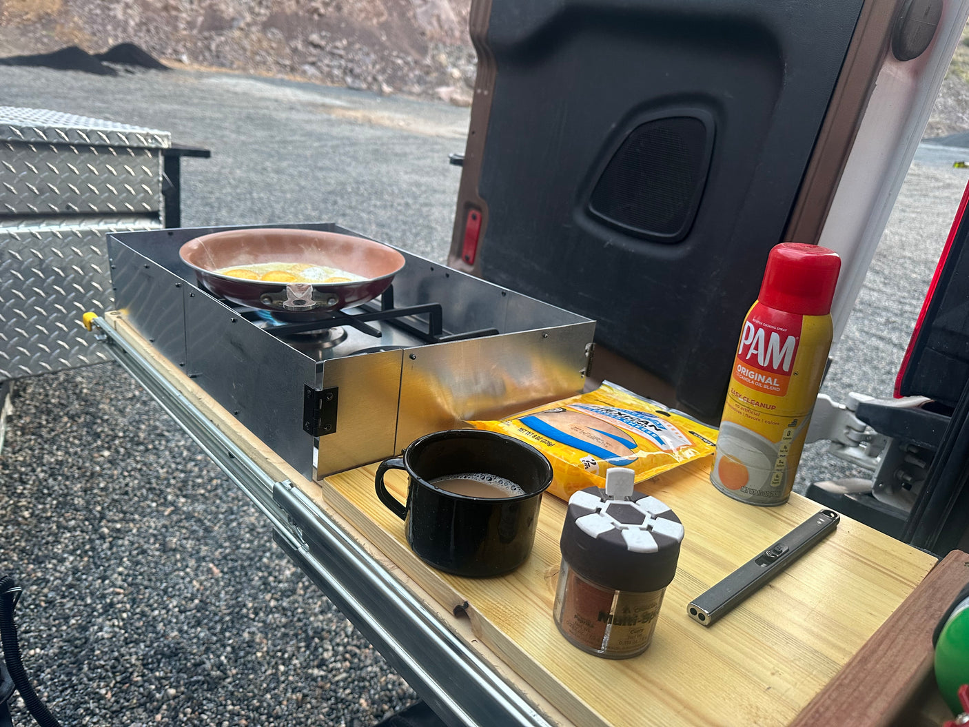 Enjoying outdoor breakfast in an RV rental. Eggs frying on a portable stove with coffee, spices, and cooking spray ready.