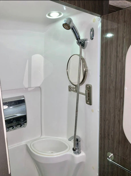 Inside an rv rental: compact shower stall with a handheld shower, sink, mirror, and soap dispenser. Space-saving design.