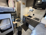 Compact RV rental interior featuring bunk beds, a cozy kitchen, and dining area, perfect for travel.