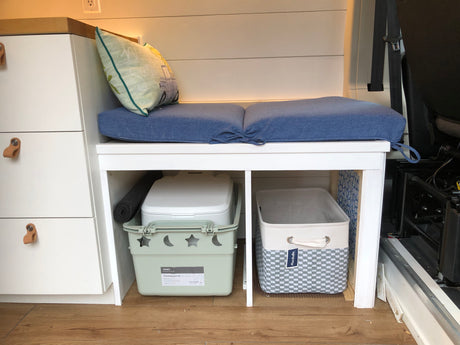 RV rental interior features a blue cushioned bench, white storage drawers, and under-bench bins, including a portable toilet.