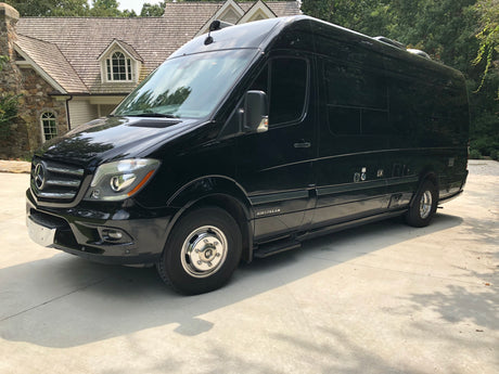 A sleek black Airstream Mercedes-Benz Sprinter RV rental, perfect for luxury road trips, is parked on a sunlit driveway.