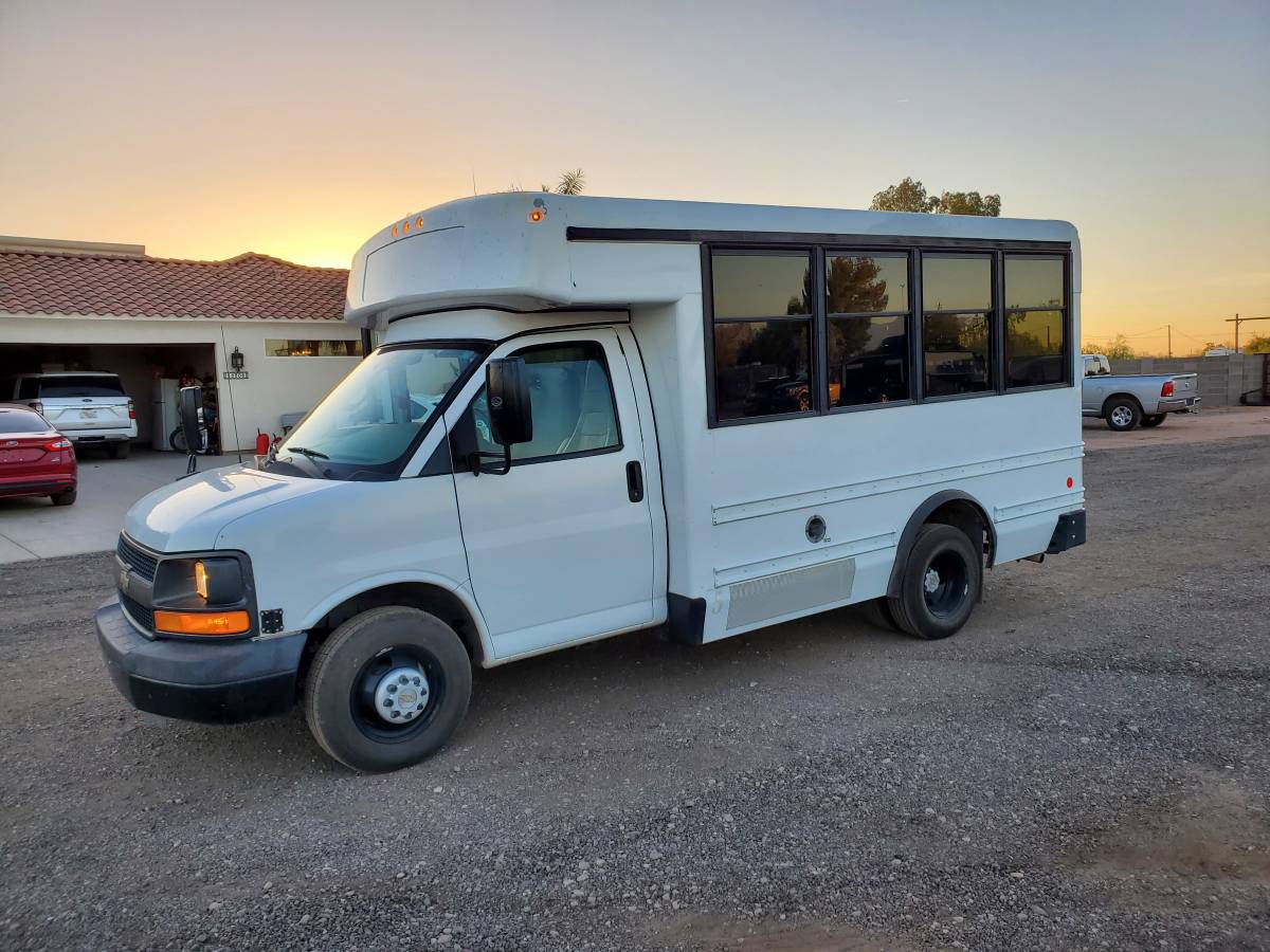 This white mini-bus, ideal for an RV rental or DIY camper conversion, is parked on gravel at sunset. — photo 9
