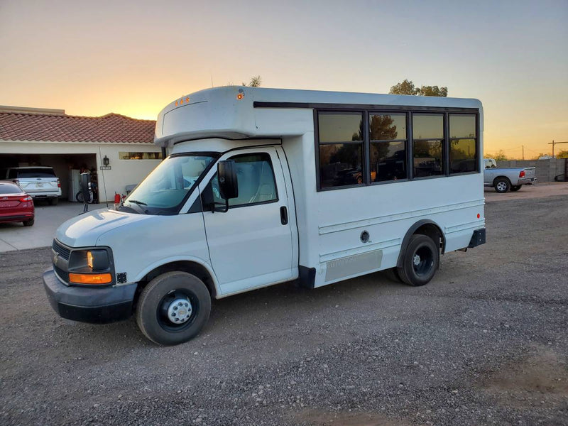 This white mini-bus, ideal for an RV rental or DIY camper conversion, is parked on gravel at sunset. — photo 9