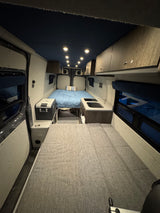 Experience mobile living! This rv rental features a cozy campervan interior with a rear bed, compact kitchen, and fridge.