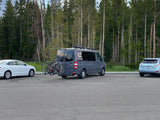 A grey RV rental camper van with bikes parked in a wooded area, ready for outdoor adventures and road trips.