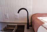 RV rental kitchenette features black faucet, white tiled backsplash, grey counter, and pink bed.