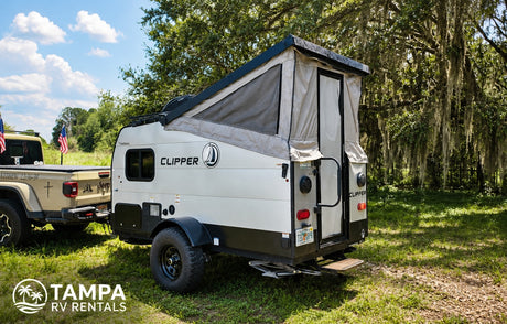 This RV rental features a pop-up camper towed by a Jeep Gladiator, parked in a sunny, grassy outdoor setting with trees. Perfect for camping.