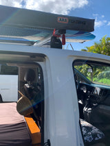 An RV rental set up for van life, featuring surfboards and an ARB awning on the roof. Its open door reveals a cozy bed inside.