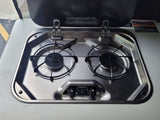Stainless steel two-burner gas stove in an RV rental kitchenette, ready for camping meals.
