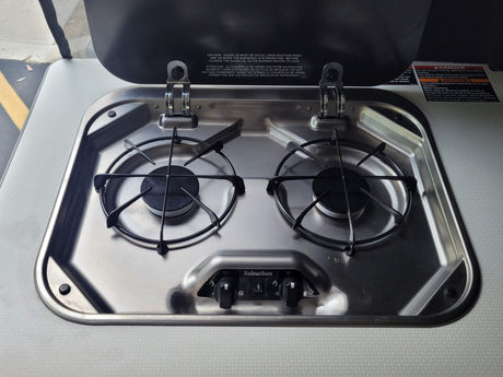 Stainless steel two-burner gas stove in an RV rental kitchenette, ready for camping meals.