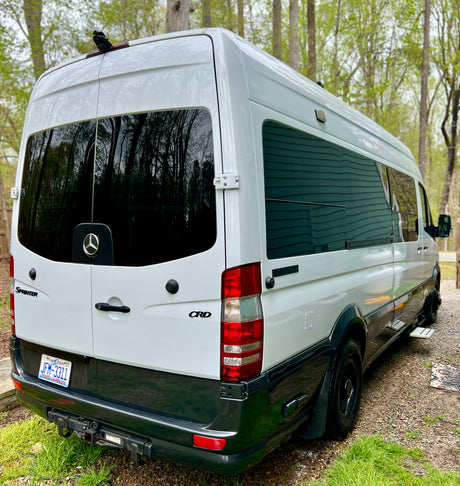 White Mercedes-Benz Sprinter van, a modern RV rental. Rear/side view of a sleek camper van with tinted windows.