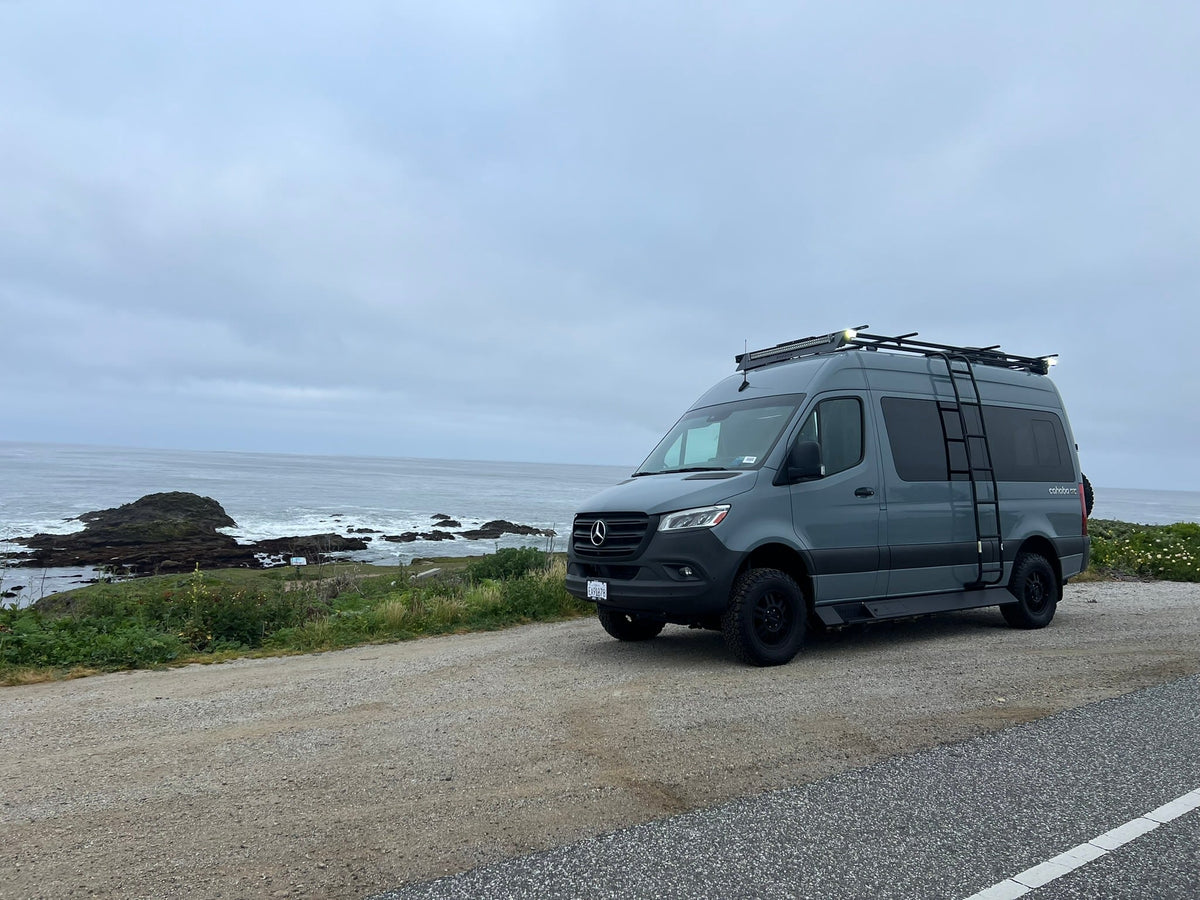 A gray Sprinter rv rental camper van is parked by a rugged
