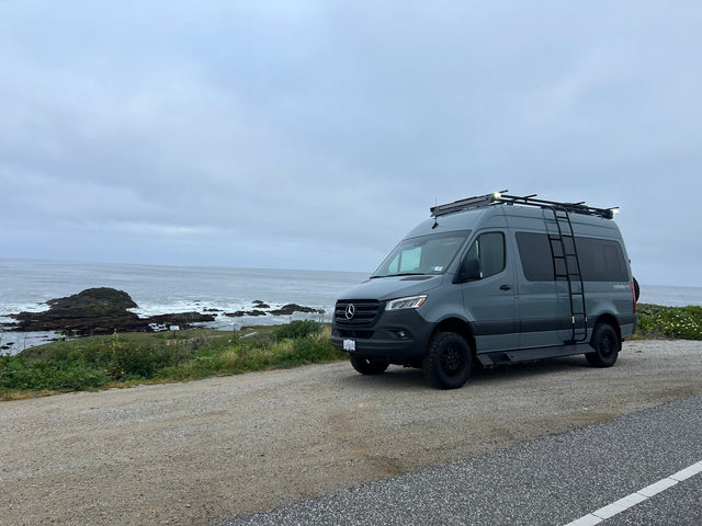 A gray Sprinter rv rental camper van is parked by a rugged