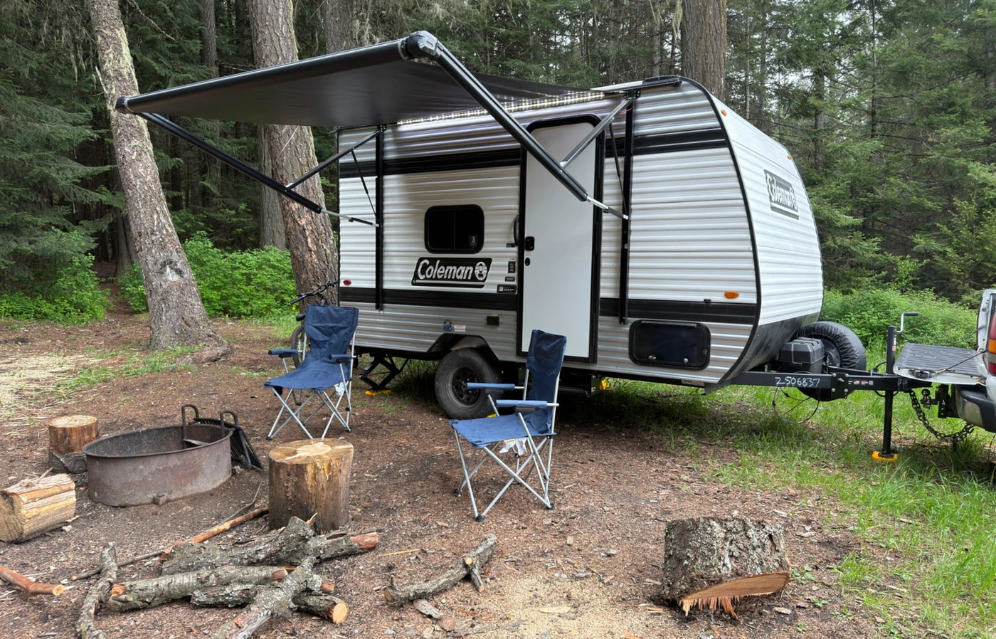 RV rental set up at a peaceful forest campsite. This small travel trailer with its awning extended is ready for camping — photo 1