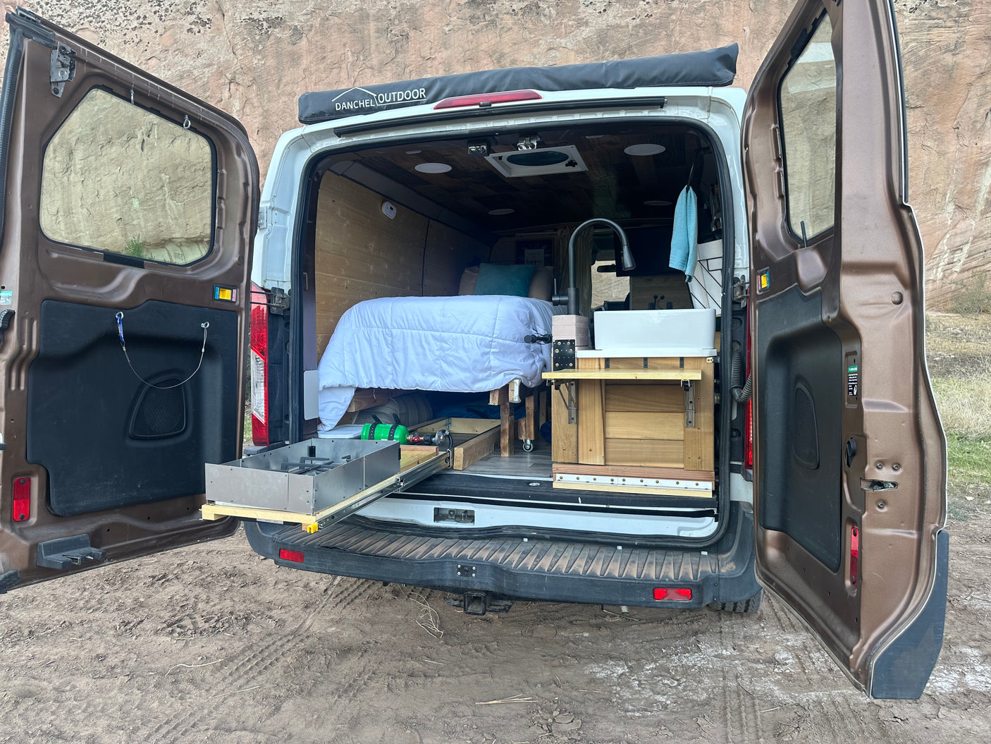 Custom RV rental camper van interior: cozy bed, pull-out kitchen with stove, and sink ready for adventures.