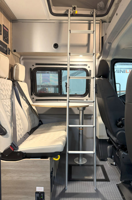 Inside an RV rental van: seating with seatbelts, a detachable table, a window, and a ladder to an upper sleeping area.