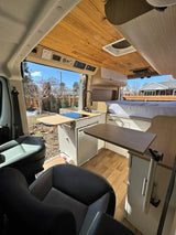 Modern RV rental interior with wooden ceiling, kitchenette, comfy bed, and swivel seats. Perfect for your next adventure!