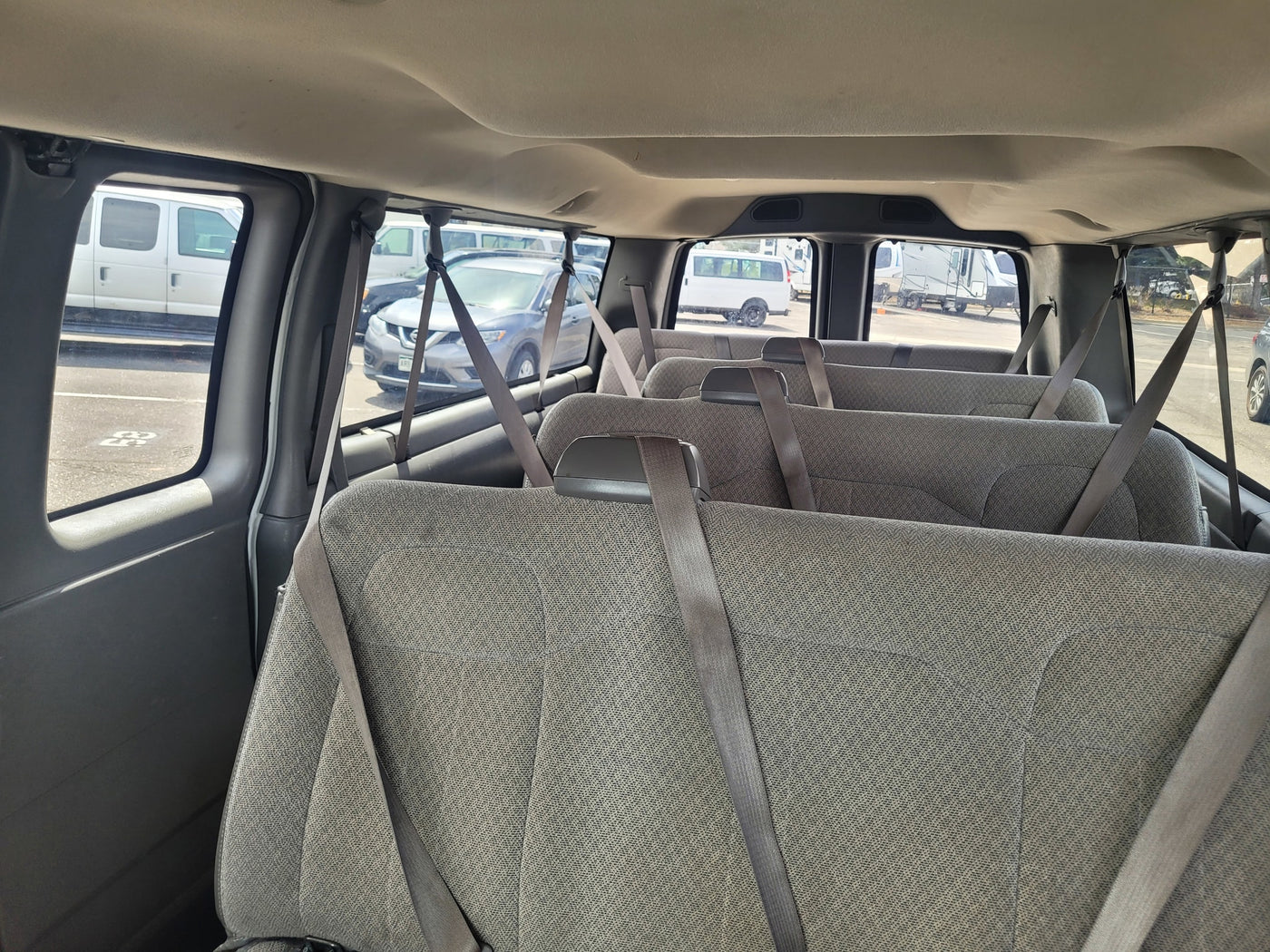 Rows of grey seats inside a passenger van, looking out at parked vans and RVs at an RV rental facility. — photo 4