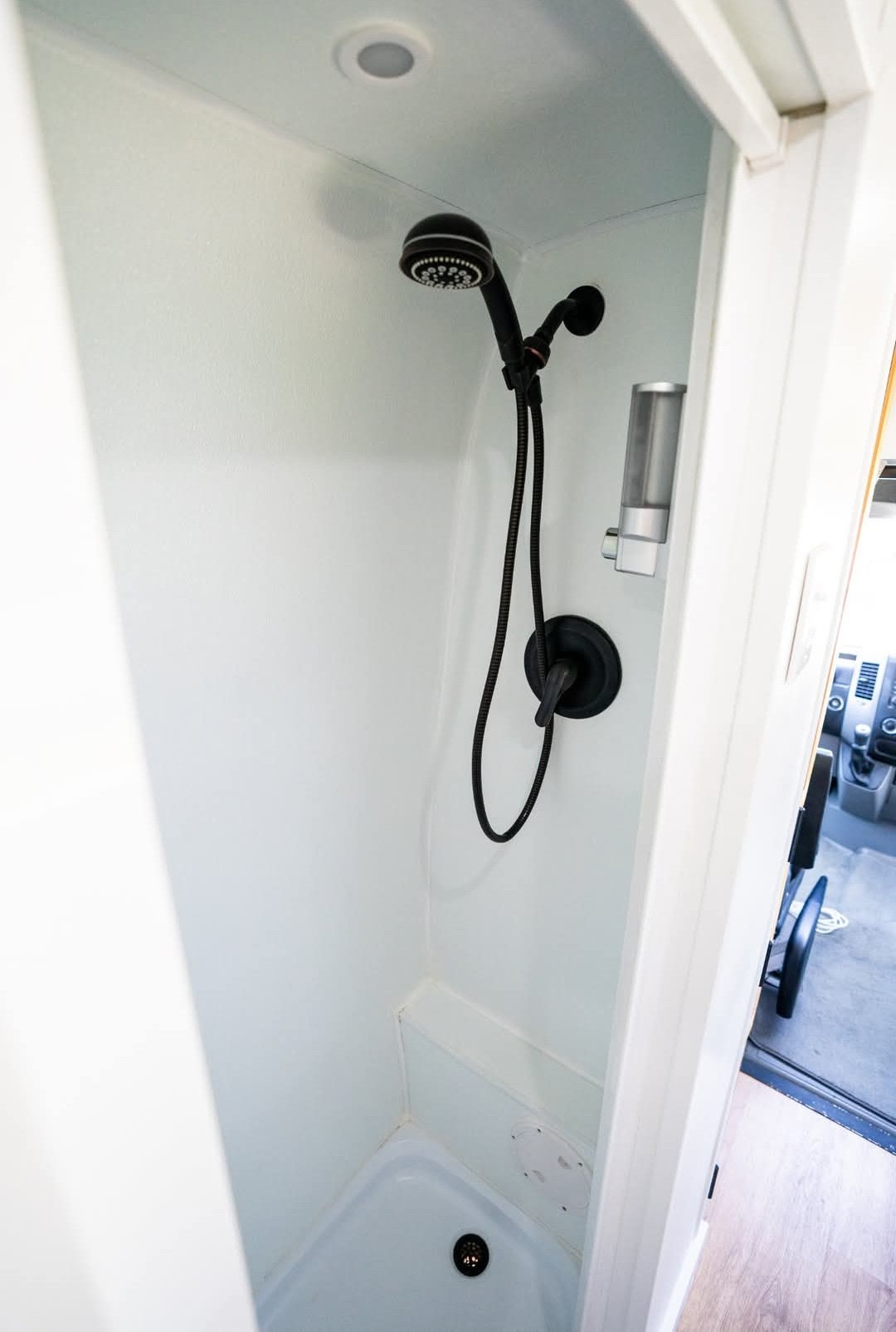 Compact RV rental shower featuring white walls, black shower head, faucet, and a wall-mounted dispenser. Perfect for road trips. — photo 10