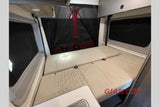 This RV rental interior shows a convertible bed with textured beige cushions, black privacy screens on windows and rear doors, and overhead cabinets.