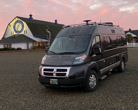 This dark gray RV rental van is parked at the Blue Heron French Cheese Company during a pink sunset. Ideal for your next trip.